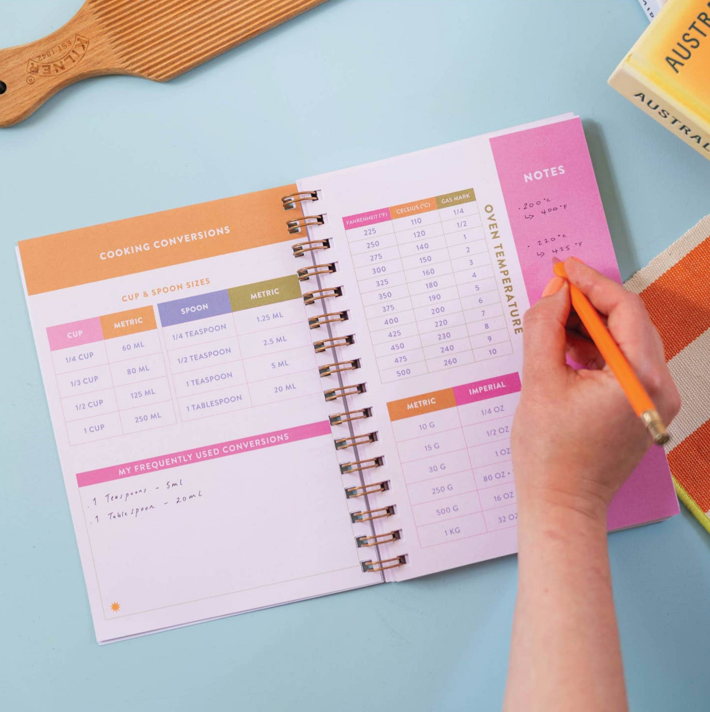Person using a spiral-bound conversion chart with a pen on a light blue surface