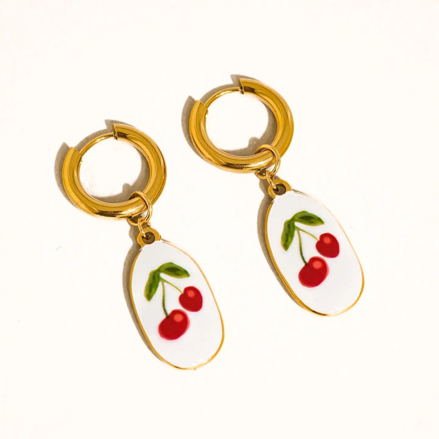 βCherry Gold Danglesβ β Close-up of vintage cherry earrings against a blush fabric background
βSweet Retro Earringsβ β Earrings styled next to red lipstick and heart sunglasses