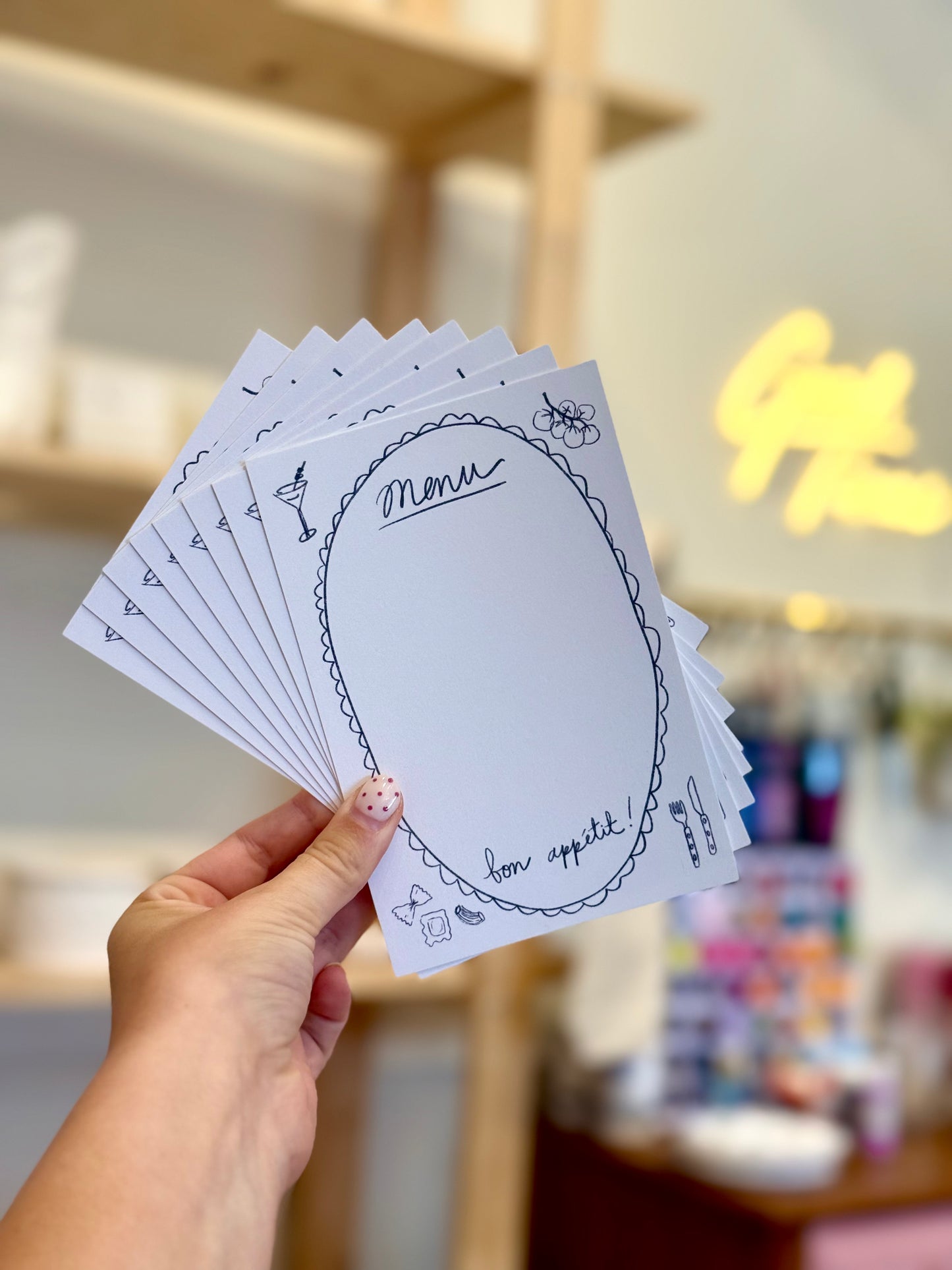 Hand holding a stack of white cards with black text and designs against a blurred indoor background