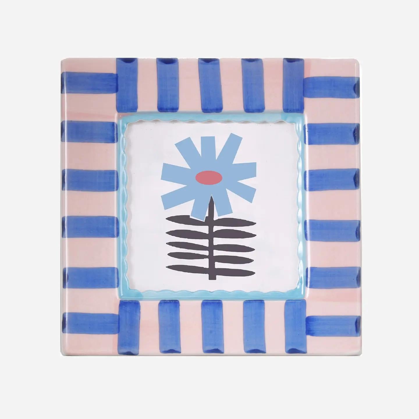 Square hand-painted ceramic photo frame with soft blue stripes on a white base.β
βClose-up of a blue-striped ceramic frame holding a small photo on a wooden shelf.β
βHand-painted blue and white ceramic frame styled beside flowers and candles.β