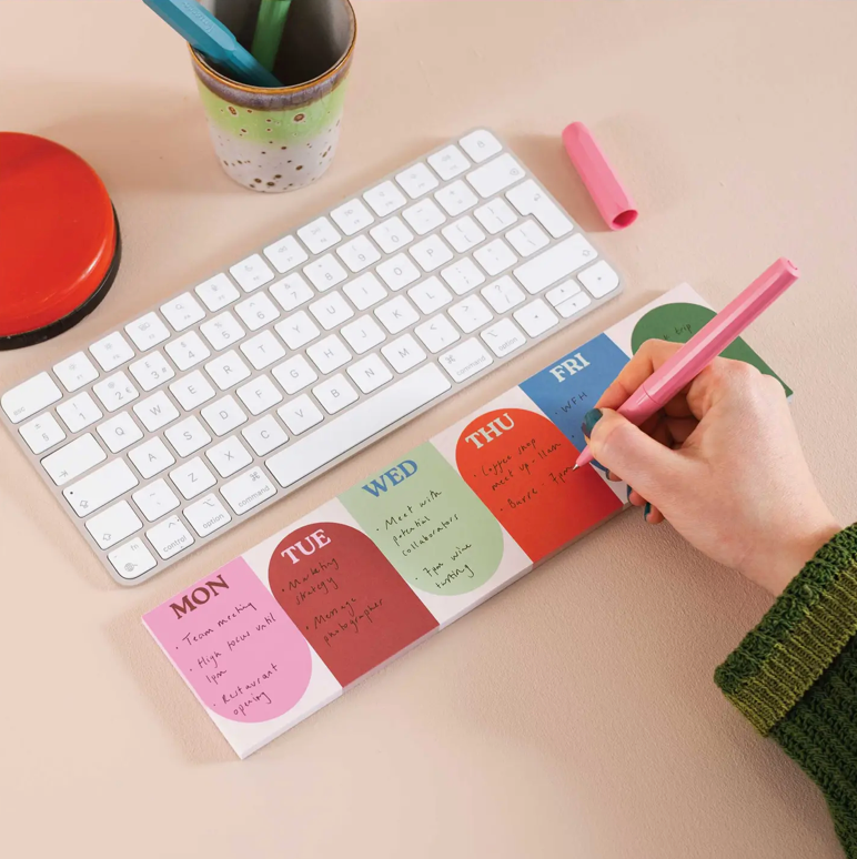 Colorful weekly planner pad on a desk with a keyboard and pen