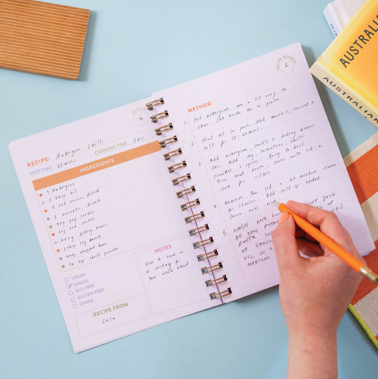 Open spiral-bound notebook with handwritten recipe on a light blue surface