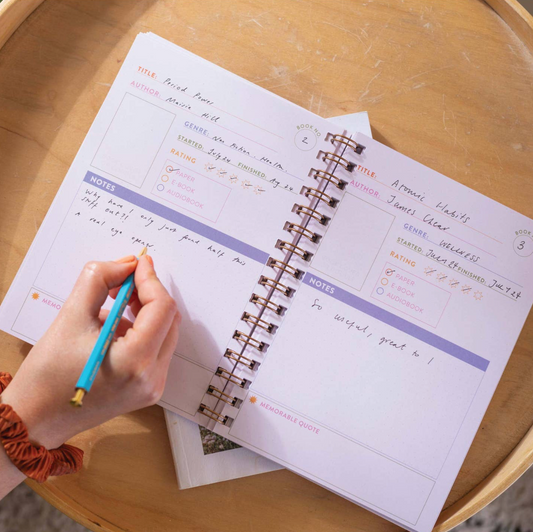 Person writing in a spiral-bound notebook on a wooden table