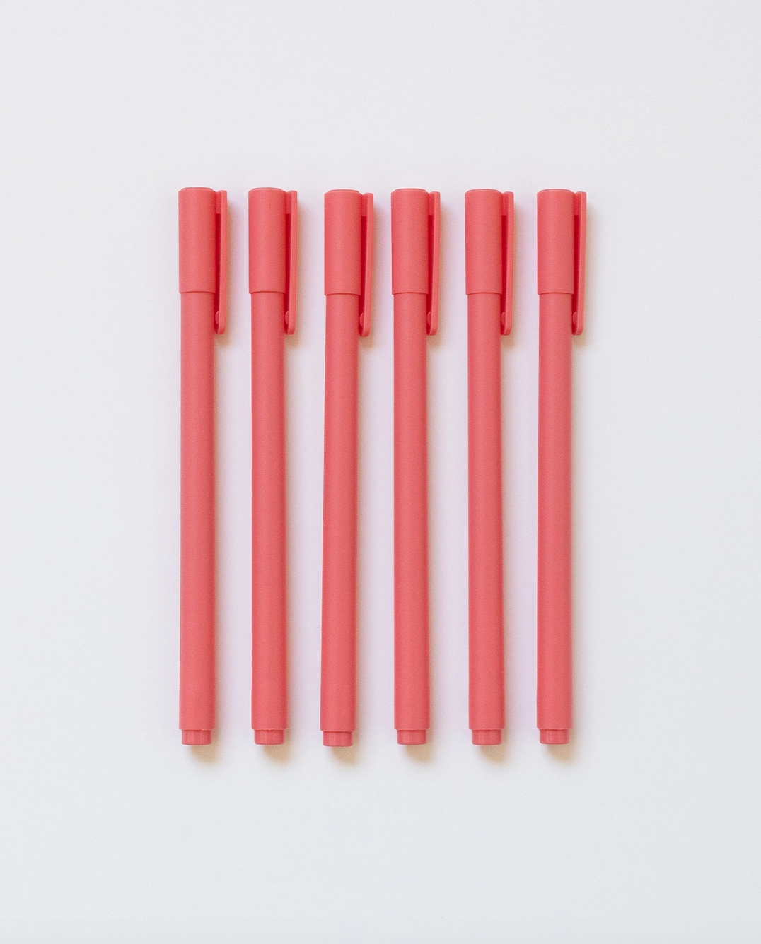 Set of eight coral-colored pens on a light gray background