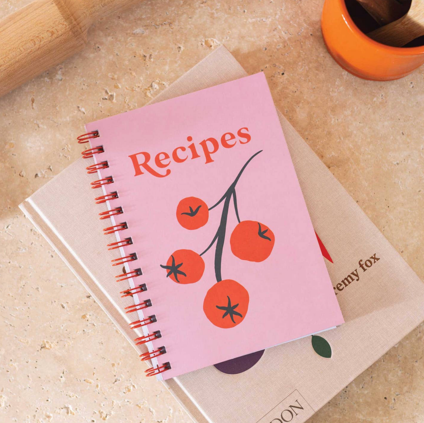 Pink recipe book with tomato design on a beige surface