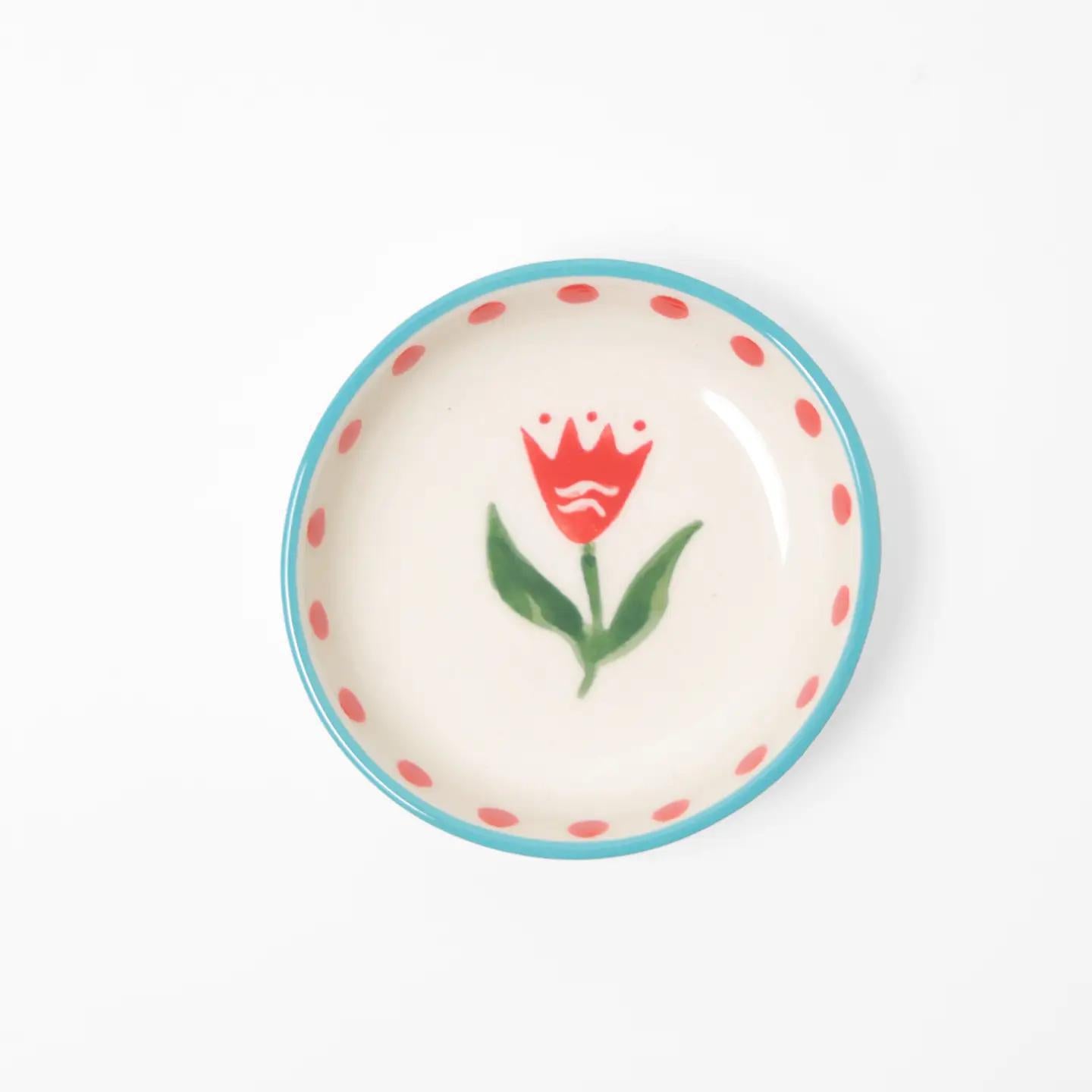 “Small hand-painted ceramic bowl with red flower design, blue rim, and red dots on white background.”
“Close-up of mini stoneware bowl holding gold jewelry, decorated with red flowers.”
“Petite hand-painted red floral bowl styled beside pink petals and a cup of tea.”