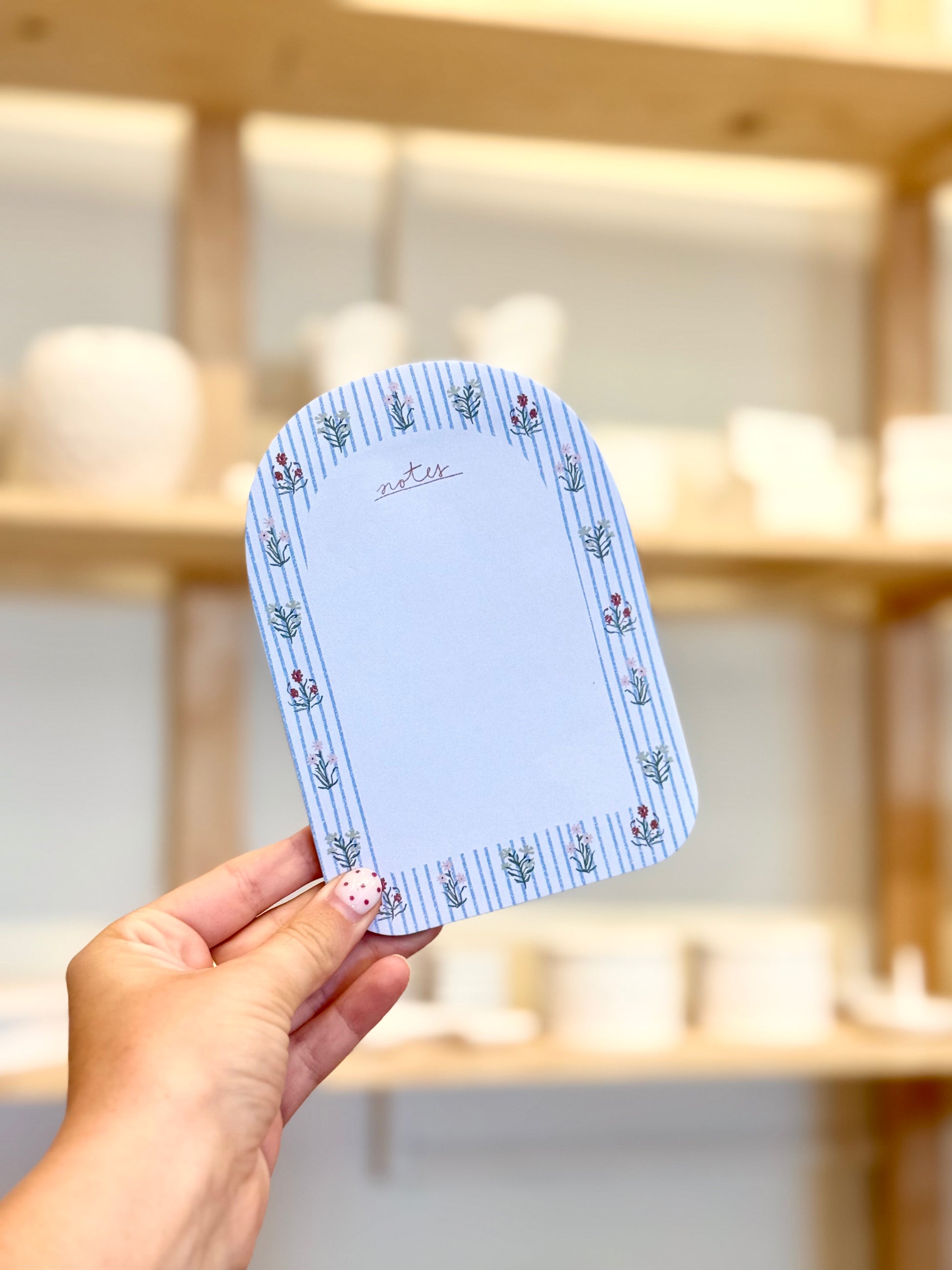 Hand holding a blue notepad with floral patterns against a blurred wooden shelf background