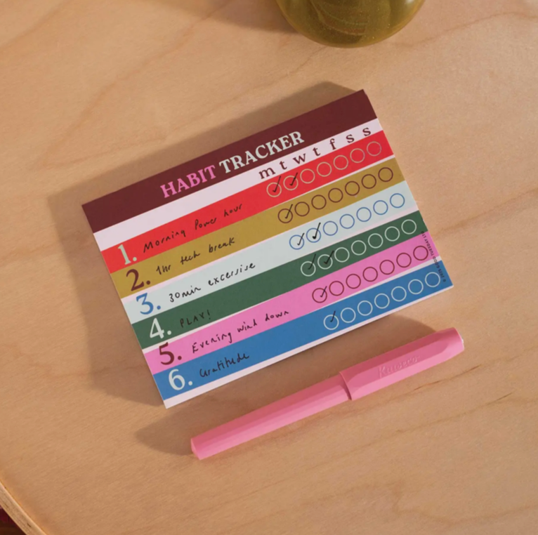 Habit tracker with colorful design on a wooden surface with a pink pen.