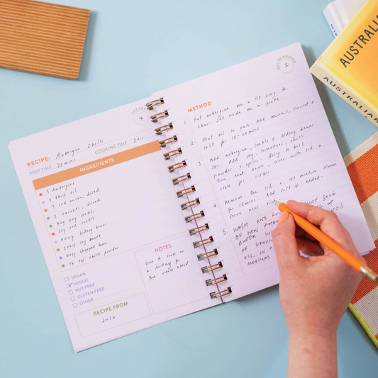 Open spiral-bound notebook with handwritten recipe on a light blue surface