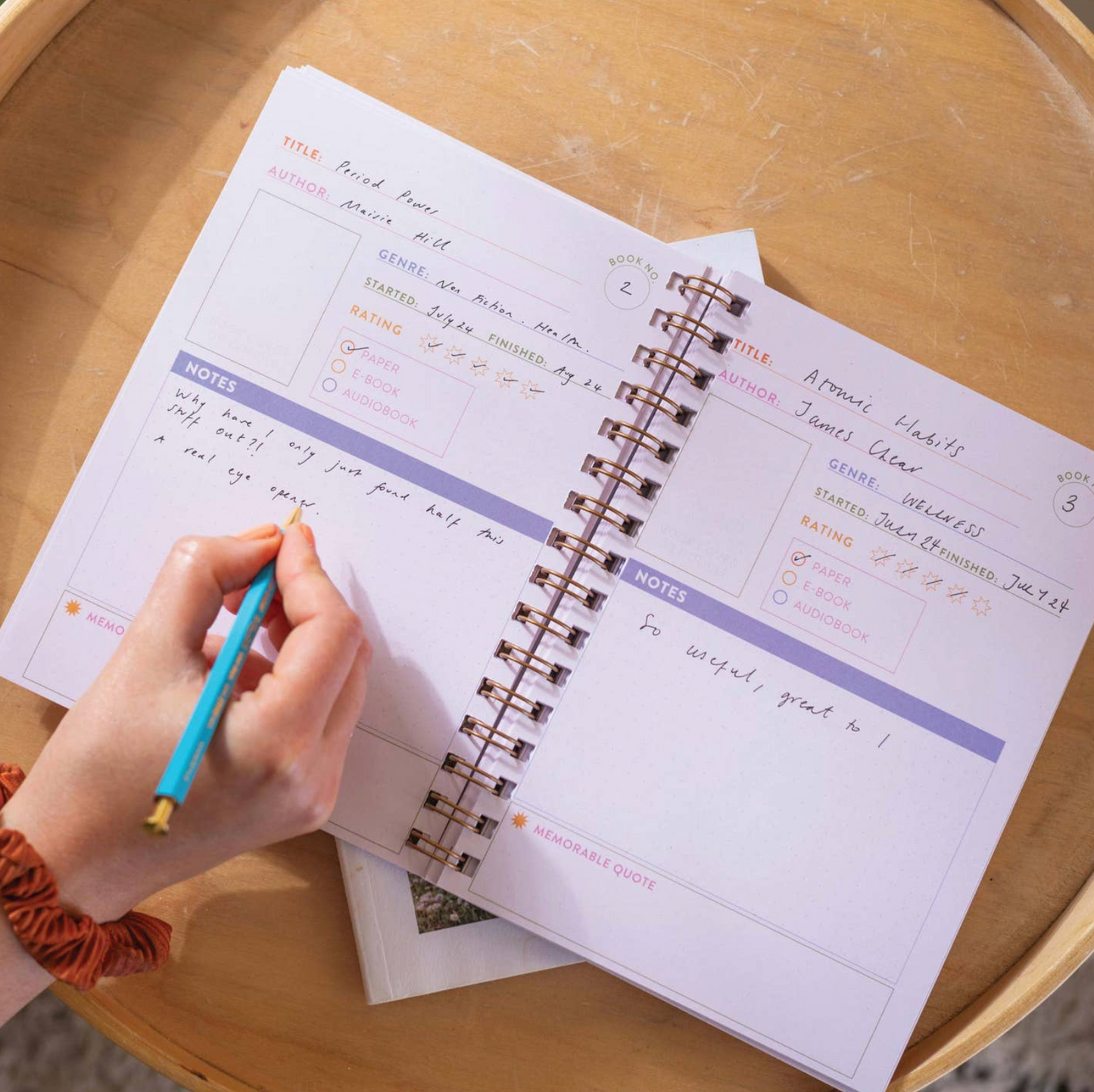 Person writing in a spiral-bound notebook on a wooden table