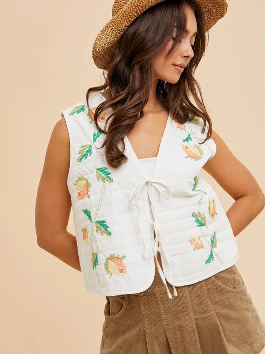 “Embroidered Bow Tie Vest” – Vest layered over a puff-sleeve blouse, styled in natural light

“Cottagecore Quilted Layer” – Vest on hanger with wildflowers and woven accessories nearby