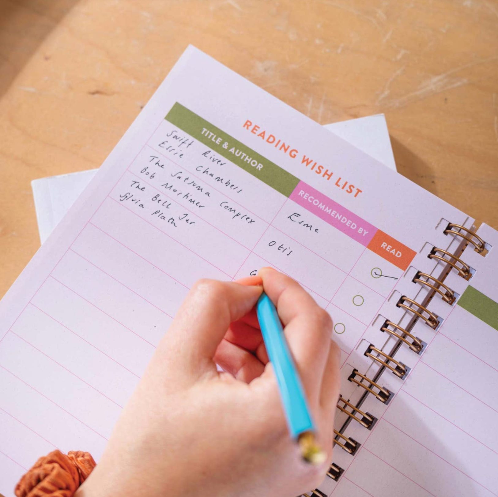 Hand writing in a planner with a pen on a wooden surface