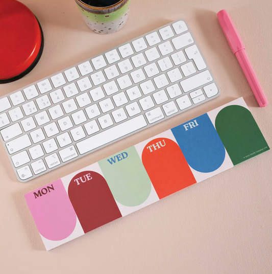 Colorful week-day planner pad next to a keyboard on a desk