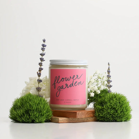 “Bloom & Glow Candle” – Flower Garden candle styled with fresh florals and greenery

“Spring in a Jar” – Close-up of lit candle surrounded by marigolds and leaves