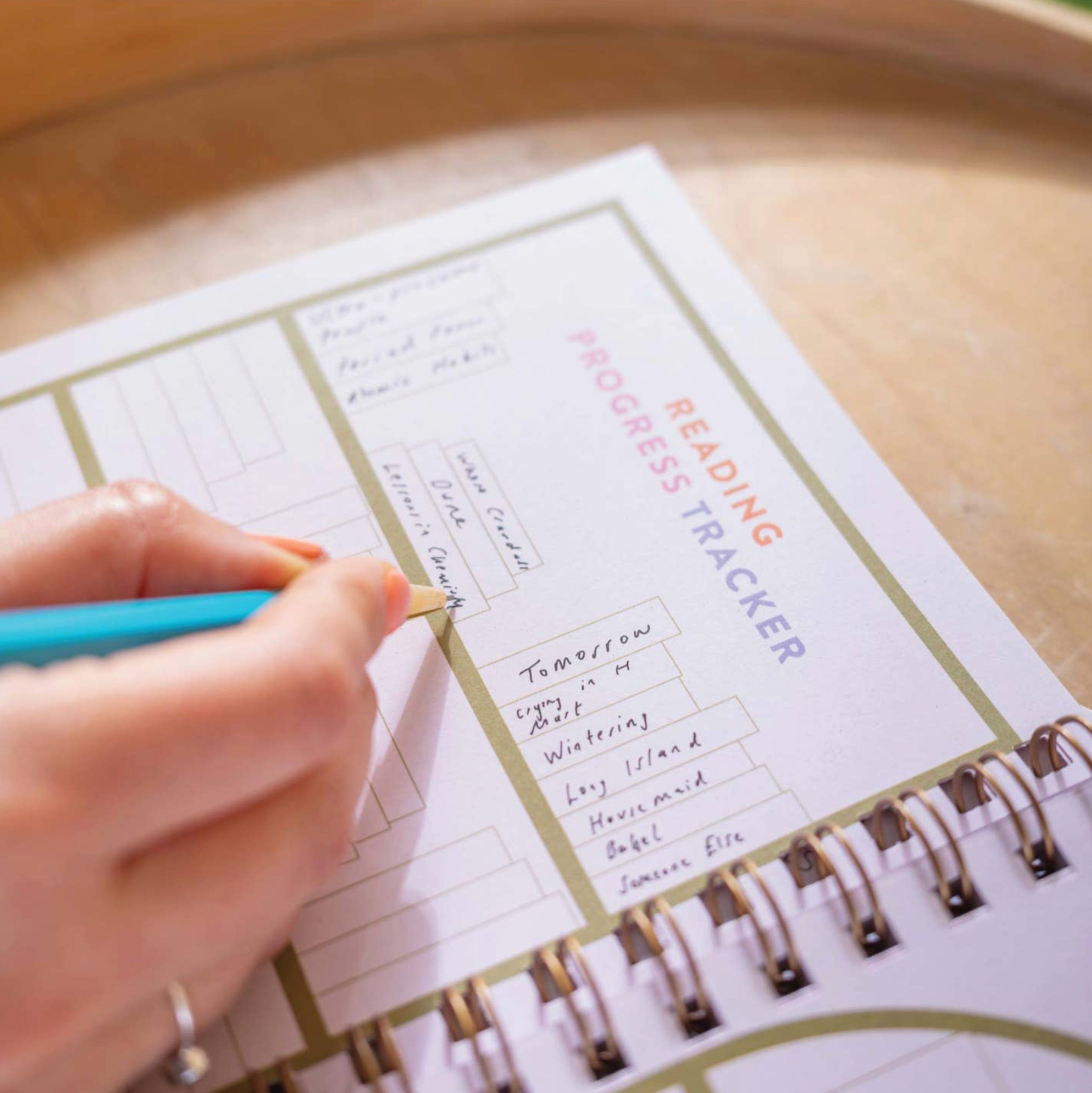 Person using a pen to fill out a 'Progress Tracker' in a planner on a wooden surface.