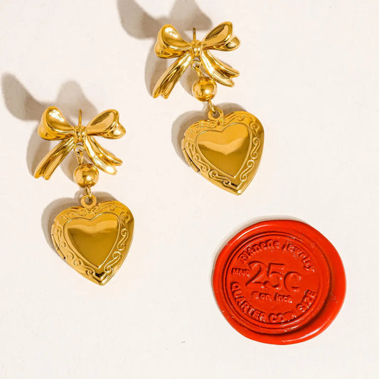 “Golden Love Drop Earrings” – Close-up of heart & bow-shaped 18K gold earrings on blush satin

“Locket Luxe Look” – Earrings styled with pastel accessories and florals for a dreamy flat lay