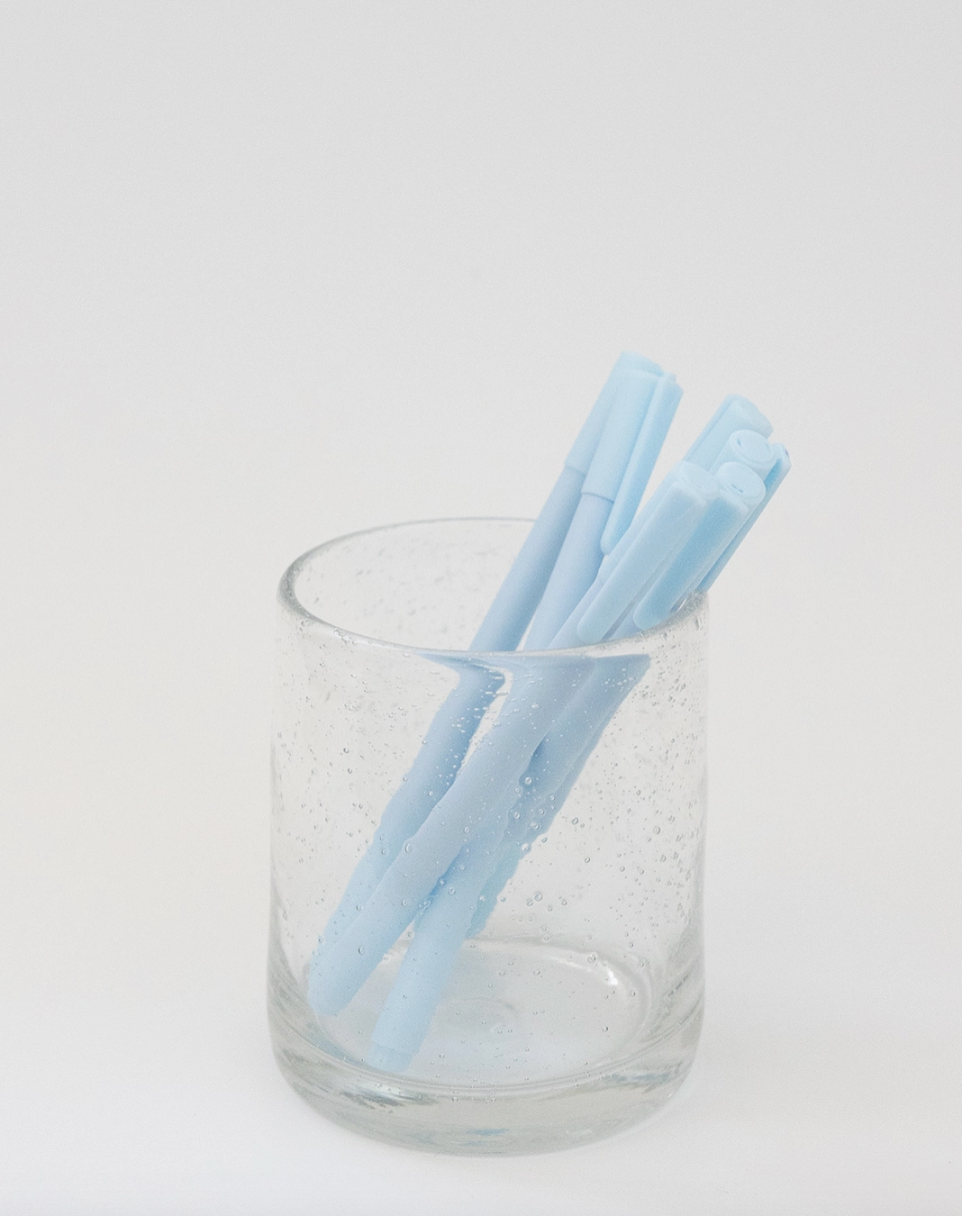 Two light blue silicone straws in a clear glass on a white background