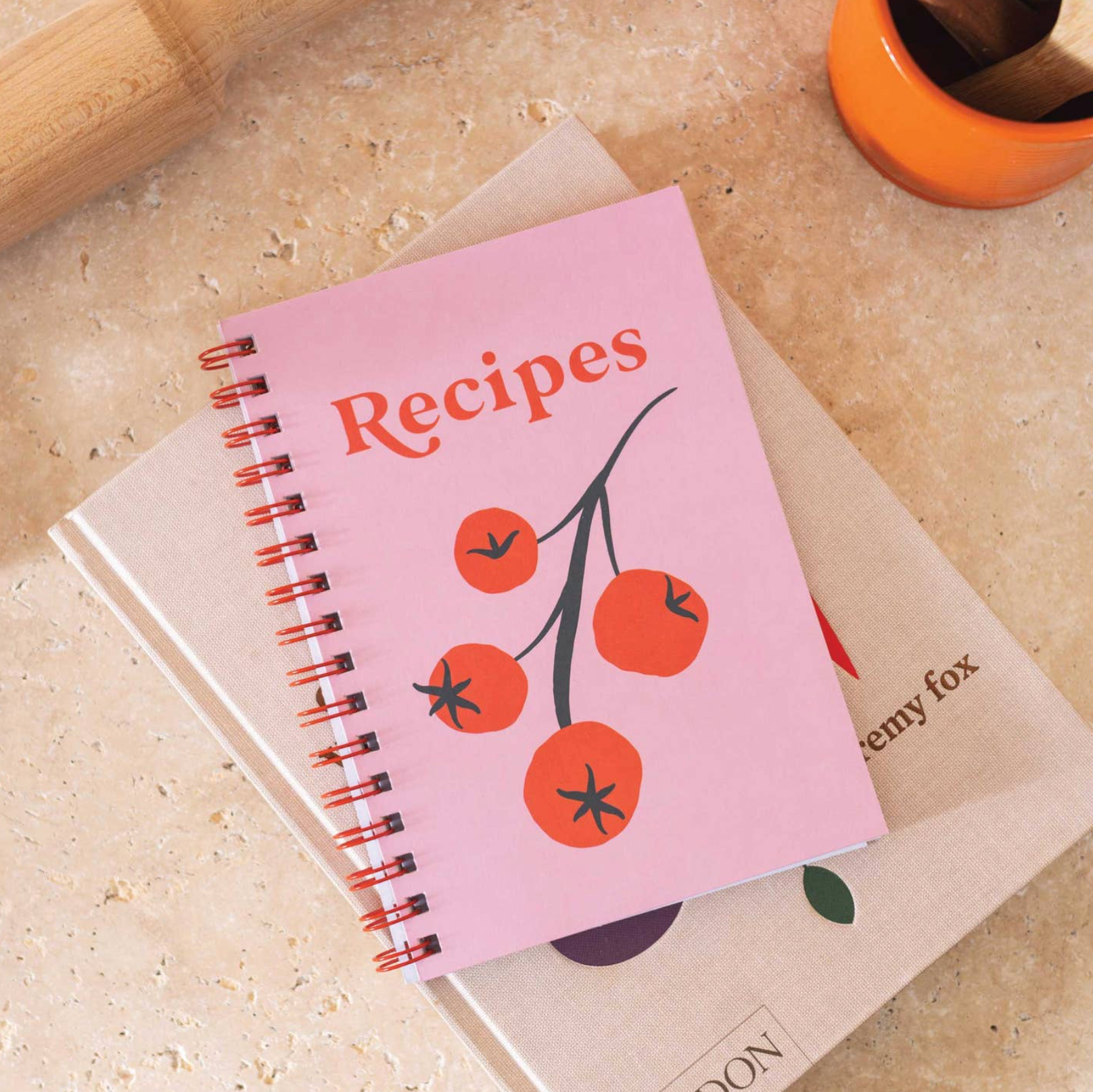 Pink recipe book with tomato design on a beige surface