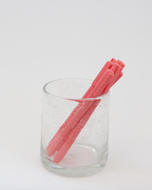Pink straws in a clear glass on a white background